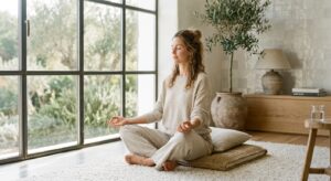 A serene, high-end editorial shot of a woman in soft neutral loungewear practicing mindful breathing
